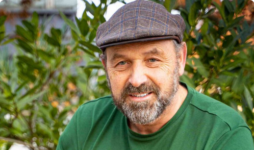 KI generiert: Ein Mann mit Bart und Mütze lächelt in die Kamera, umgeben von grüner Vegetation.