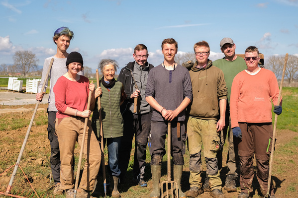 KI generiert: Eine Gruppe von acht Menschen steht mit Gartenwerkzeugen auf einem Feld.