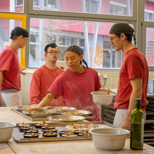 KI generiert: Menschen in roter Kleidung backen in einer Küche Pizzen.