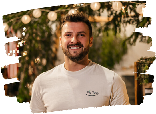 KI generiert: Ein Mann in einem weißen Shirt mit "Flo Tea"-Logo, lächelt vor einem unscharfen, beleuchteten Hintergrund.