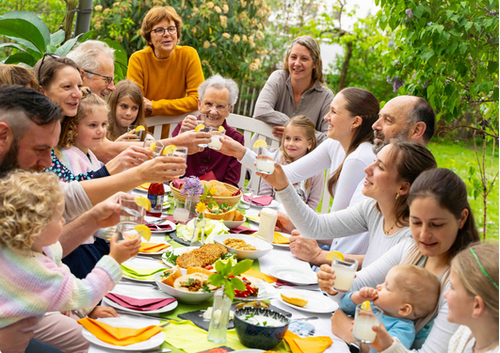 KI generiert: Eine große Familie stößt fröhlich an einem Esstisch im Garten an.