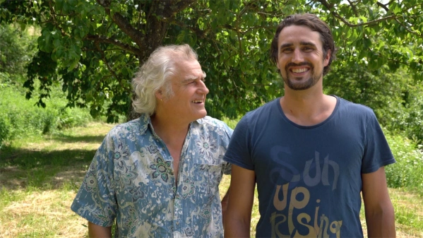 KI generiert: Zwei lächelnde Männer stehen draußen unter einem Baum. Der Text auf dem T-Shirt des rechten Mannes lautet: "Sun Up Rising".
