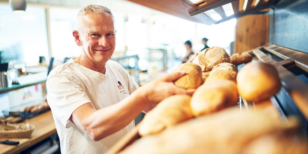 KI generiert: Ein Bäcker präsentiert frische Brote in einer Bäckerei.