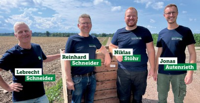 KI generiert: Vier Männer posieren lächelnd auf einem Feldweg; sie tragen dunkle T-Shirts.