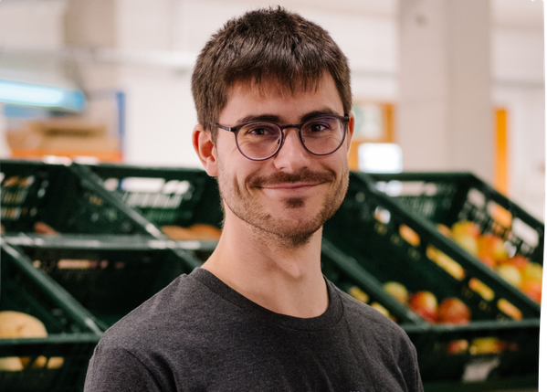 KI generiert: Ein Mann mit Brille lächelt vor leeren grünen Obstkisten in einem Geschäft.
